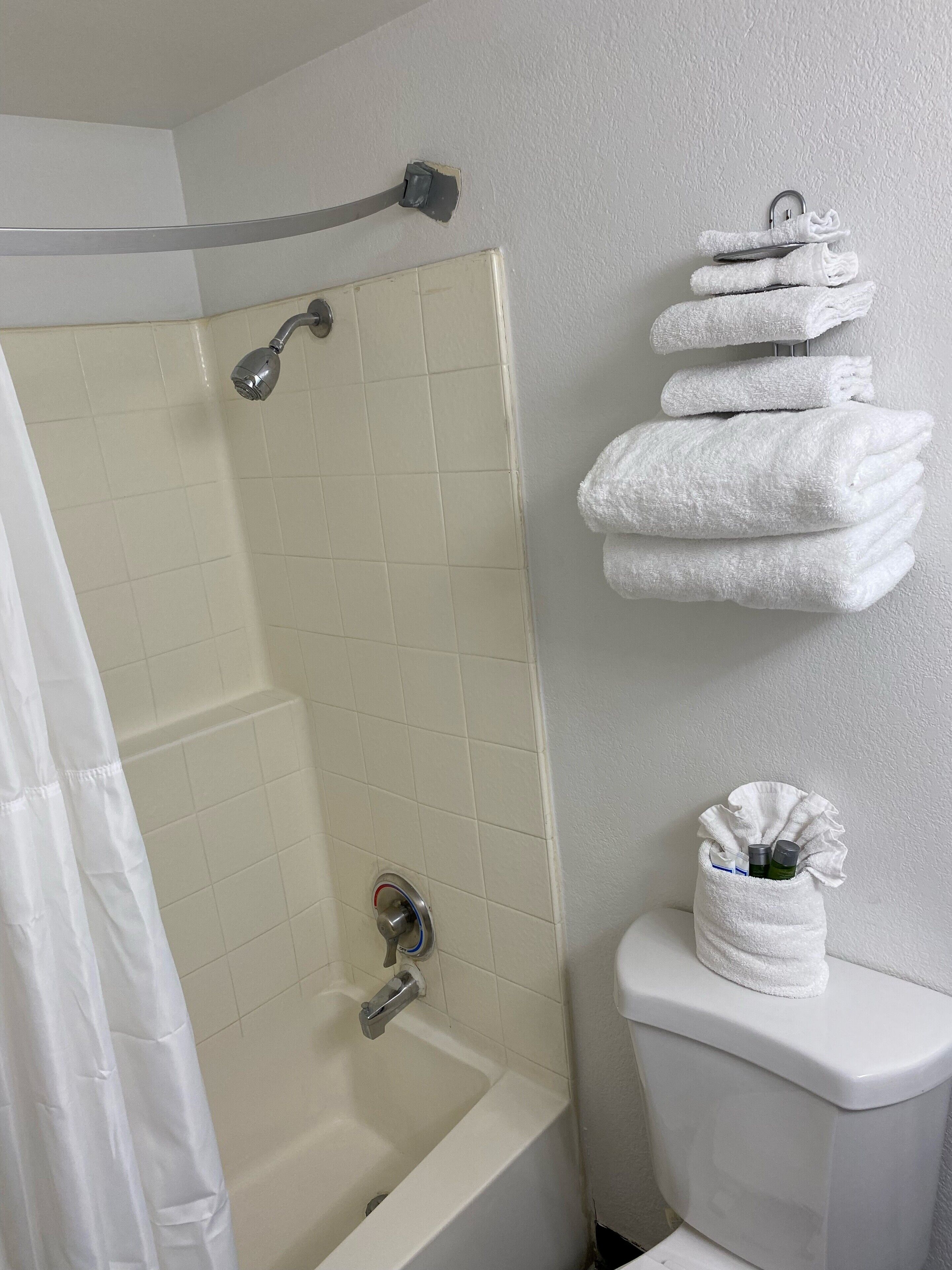 Un baño con ducha, inodoro y una pila de toallas blancas en la pared.