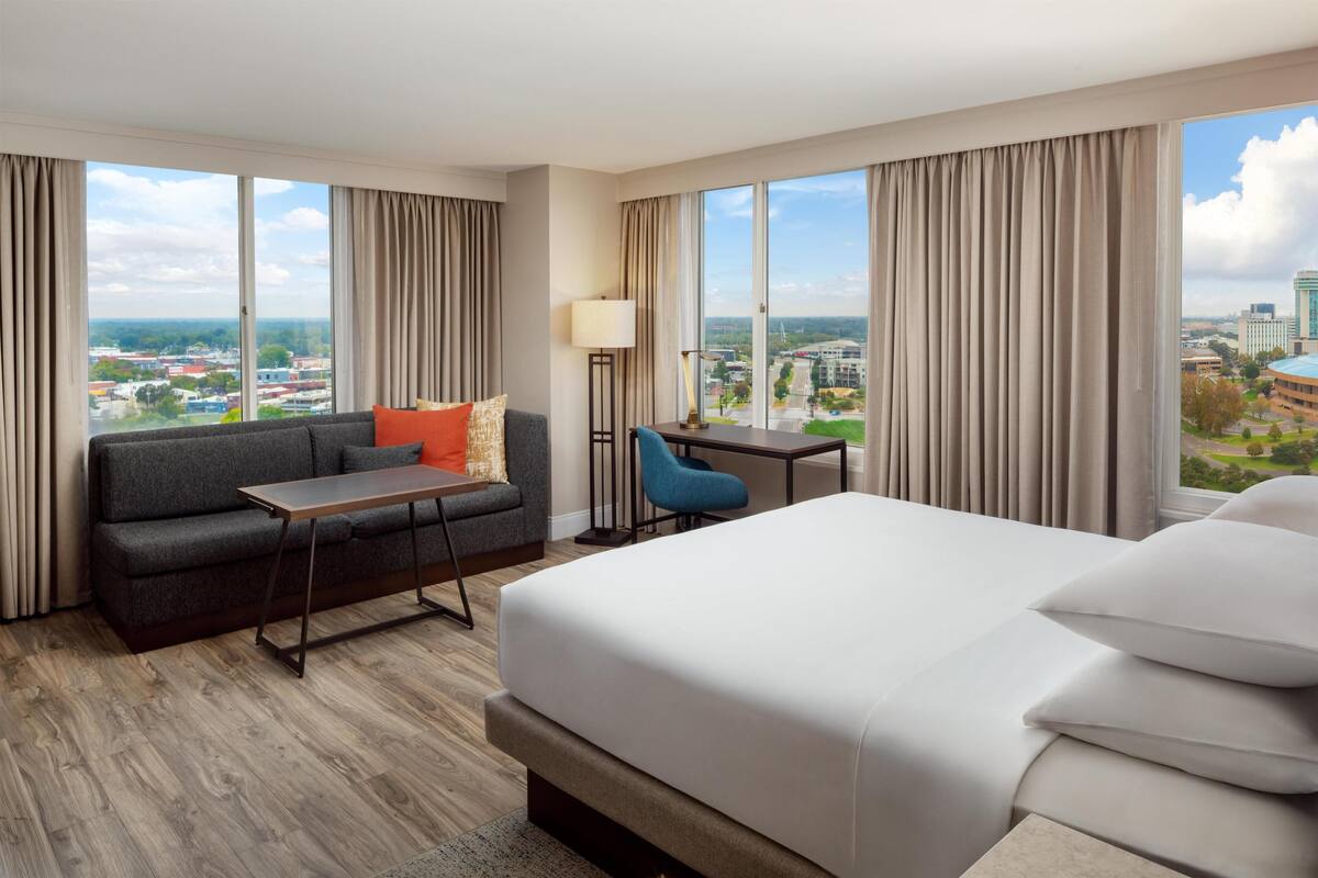 Ein Hotelzimmer mit Bett, Sofa, Schreibtisch und Blick auf die Stadt.