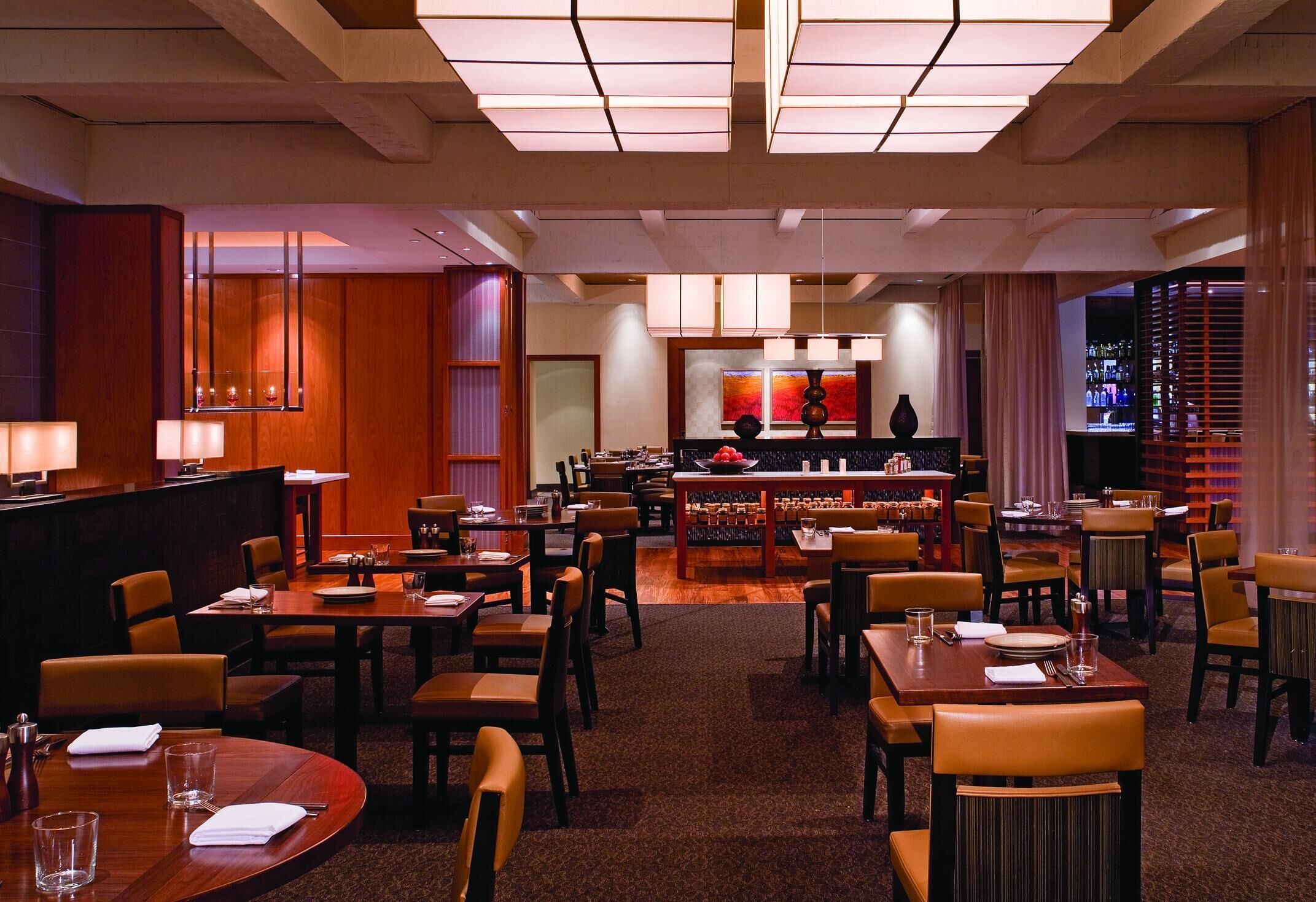 Un comedor de hotel con varias mesas y sillas, una zona de bar y un mostrador de recepción.