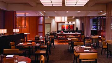 Un comedor de hotel con varias mesas y sillas, una zona de bar y un mostrador de recepción.