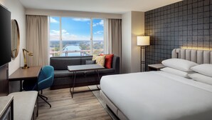 A hotel room with a large bed, a desk with a chair, a sofa, a TV, and a view of a body of water and bridge. - Hyatt Regency Wichita (Wichita)