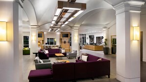 A spacious lobby with a sectional sofa, armchairs, and a coffee table. There is a reception desk with a computer and a plant. - Hyatt Regency Wichita (Wichita)