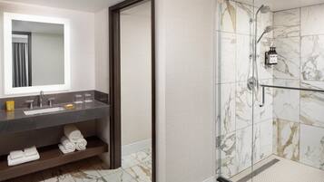 A modern bathroom with a marble shower, a large mirror, and a dark countertop with a sink and towel storage.
