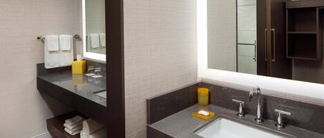 A modern bathroom with a large mirror, dark marble countertop, and a built-in shelf with towels.