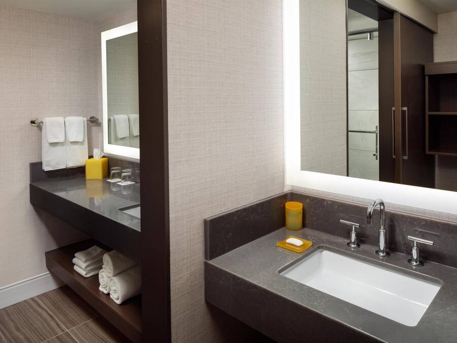A modern bathroom with a large mirror, dark marble countertop, and a built-in shelf with towels.