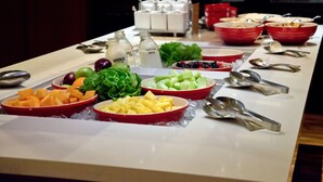 A buffet table with various fruits and vegetables, including melon, pineapple, and leafy greens, arranged on ice.