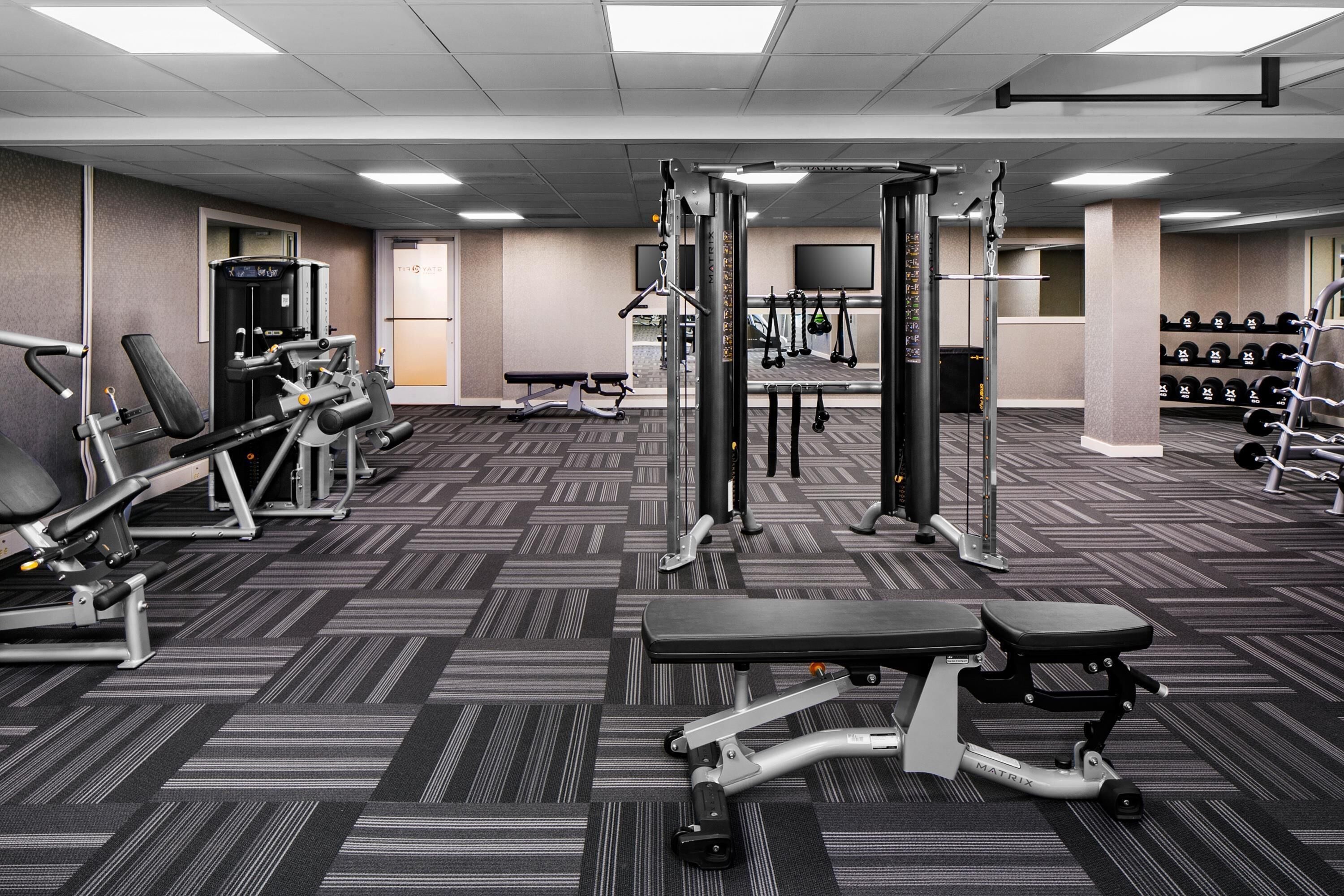 A gym with various exercise equipment, a bench, and a wall-mounted TV.