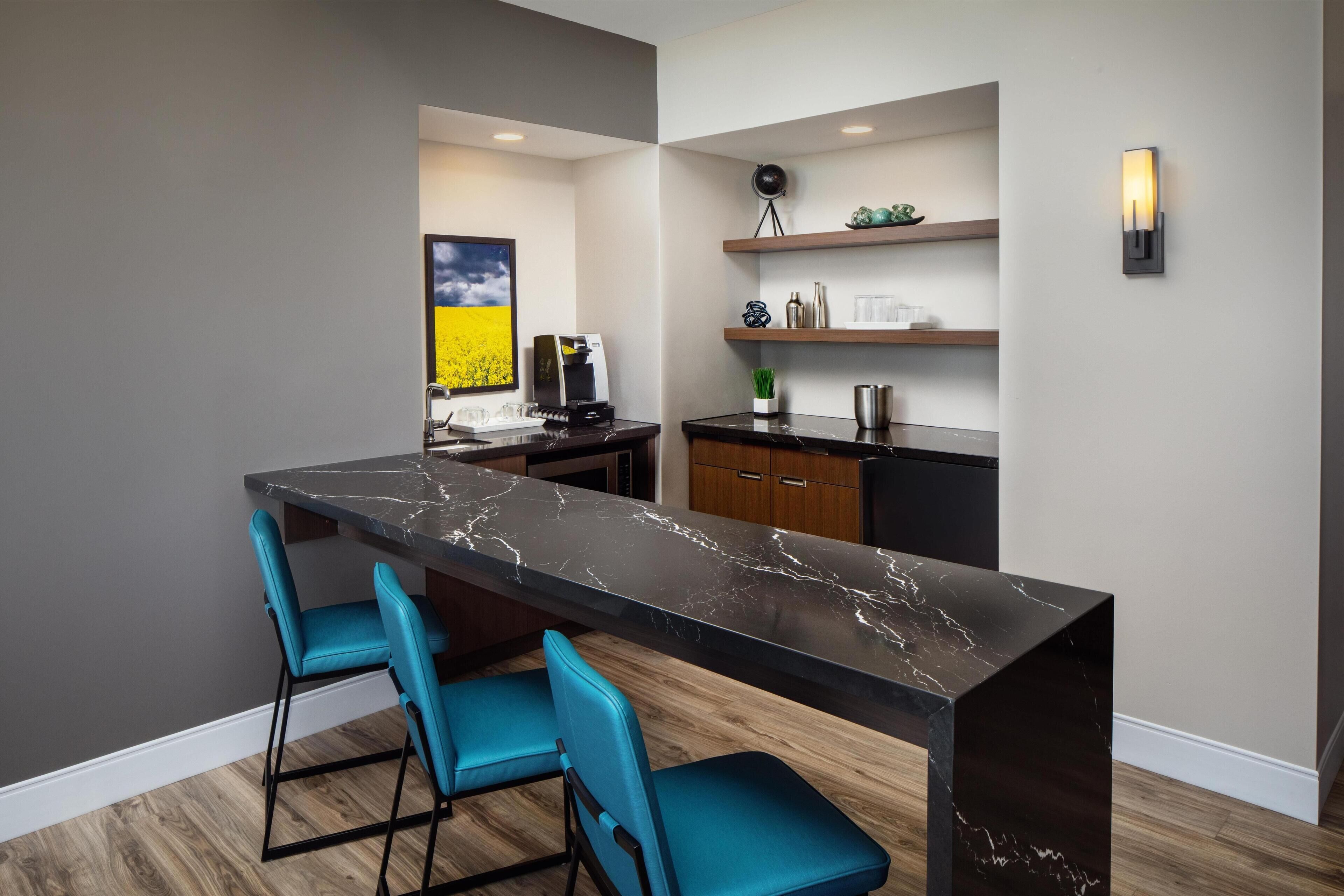 A modern kitchen with a marble countertop, teal chairs, and wooden cabinets.