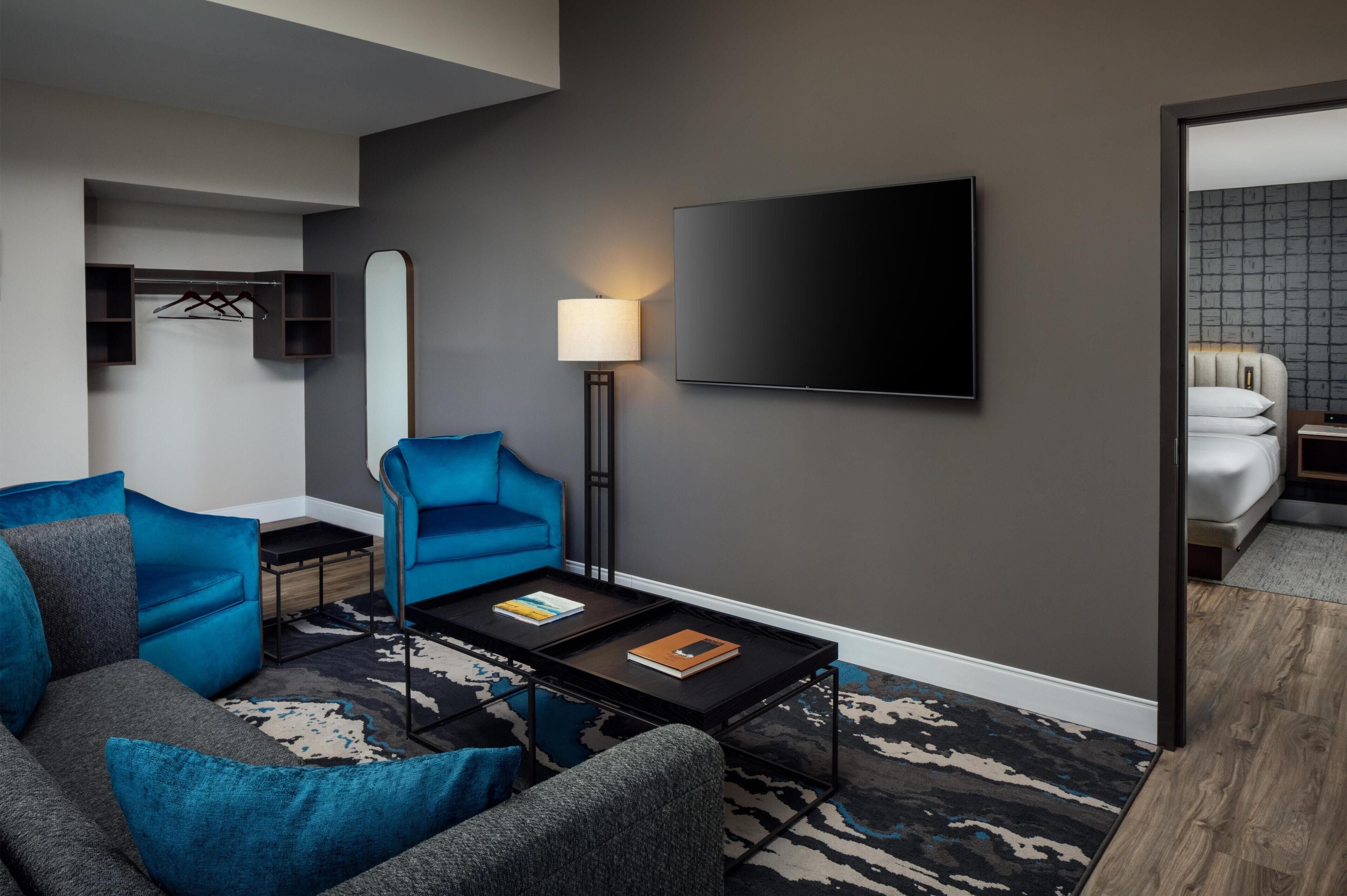 A modern hotel room with a large flat-screen TV, a sofa, a coffee table, and a lamp.