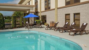 A pool area with lounge chairs and umbrellas, a clear blue pool, and a building with large windows and a flat roof. - Hampton Inn Tuscaloosa-East (Cottondale)