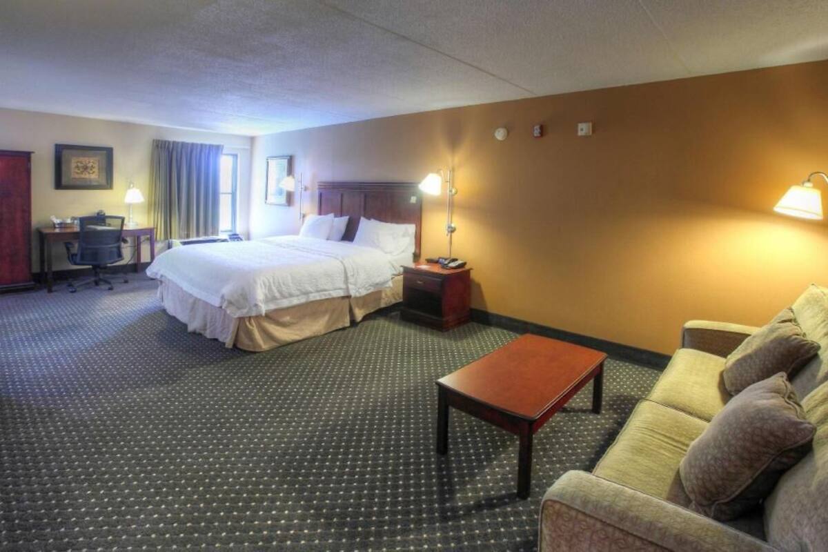 Ett hotellrum med en säng, ett skrivbord, en stol, en soffa och två sänglampor.