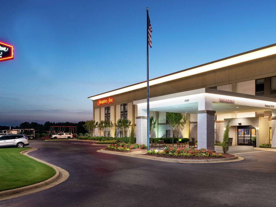 A Hampton Inn by Hilton with a well-lit entrance, parking area, and landscaped garden.