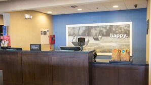 A hotel reception desk with a digital kiosk, a framed photo with the word "happy" on the wall, and a sign indicating Hilton Honors. - Hampton Inn Tuscaloosa-East (Cottondale)