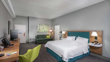 A hotel room with a bed, desk, chair, TV, and artwork on the walls.