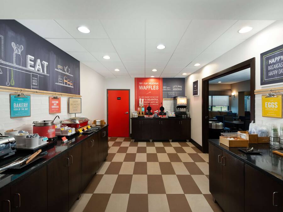 A breakfast area with a checkered floor, a red door, and various breakfast items displayed on counters.