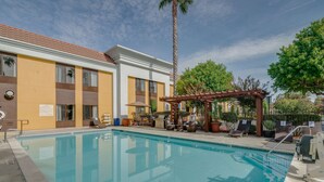 Une piscine dotée de chaises longues et d’une pergola, le tout entouré d’un bâtiment avec un toit en tuiles et d’un palmier.