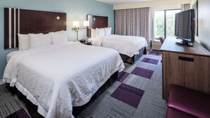 Une chambre d’hôtel avec deux lits, un bureau, une télévision et une fenêtre avec des rideaux.