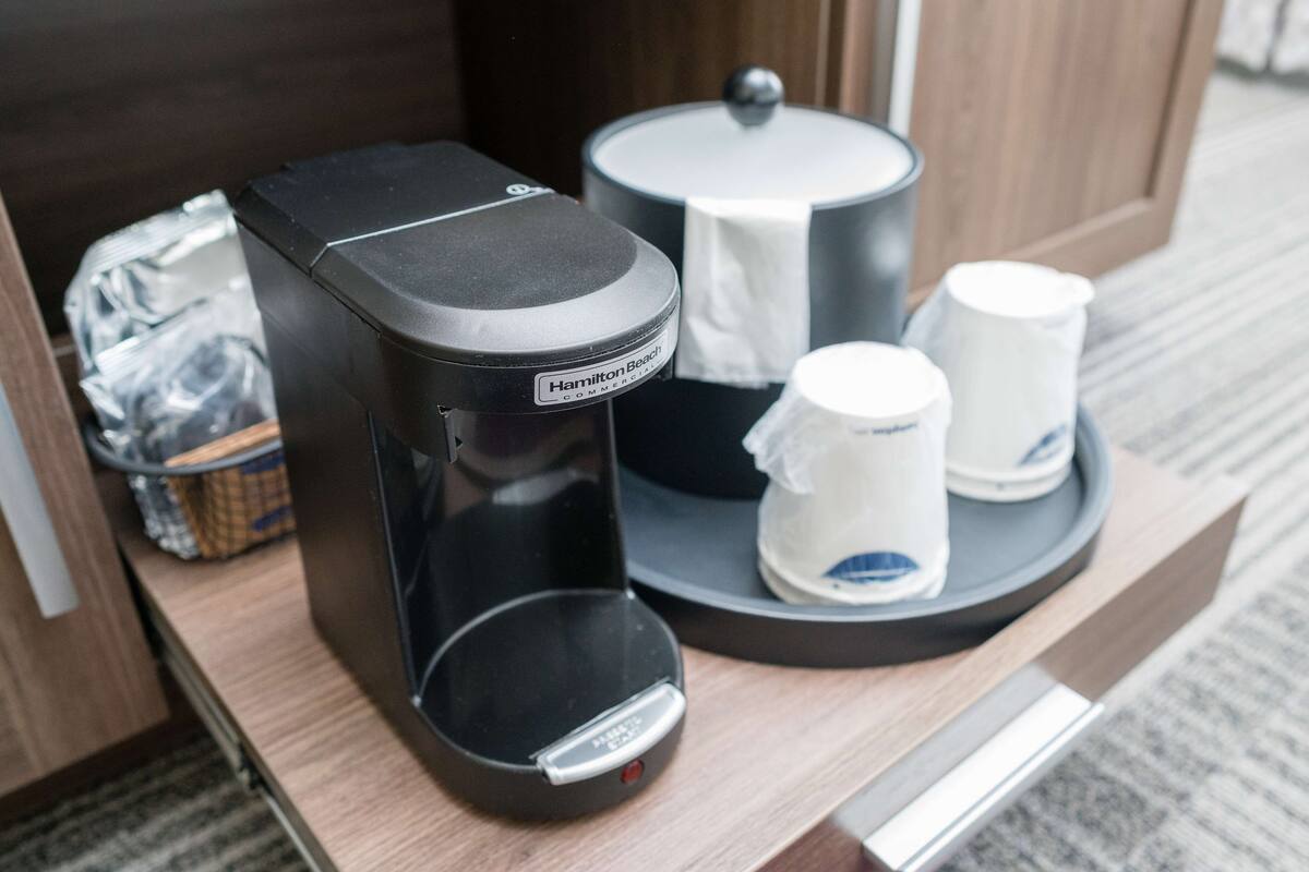 A coffee maker, a pot, and two cups on a tray in a hotel room.