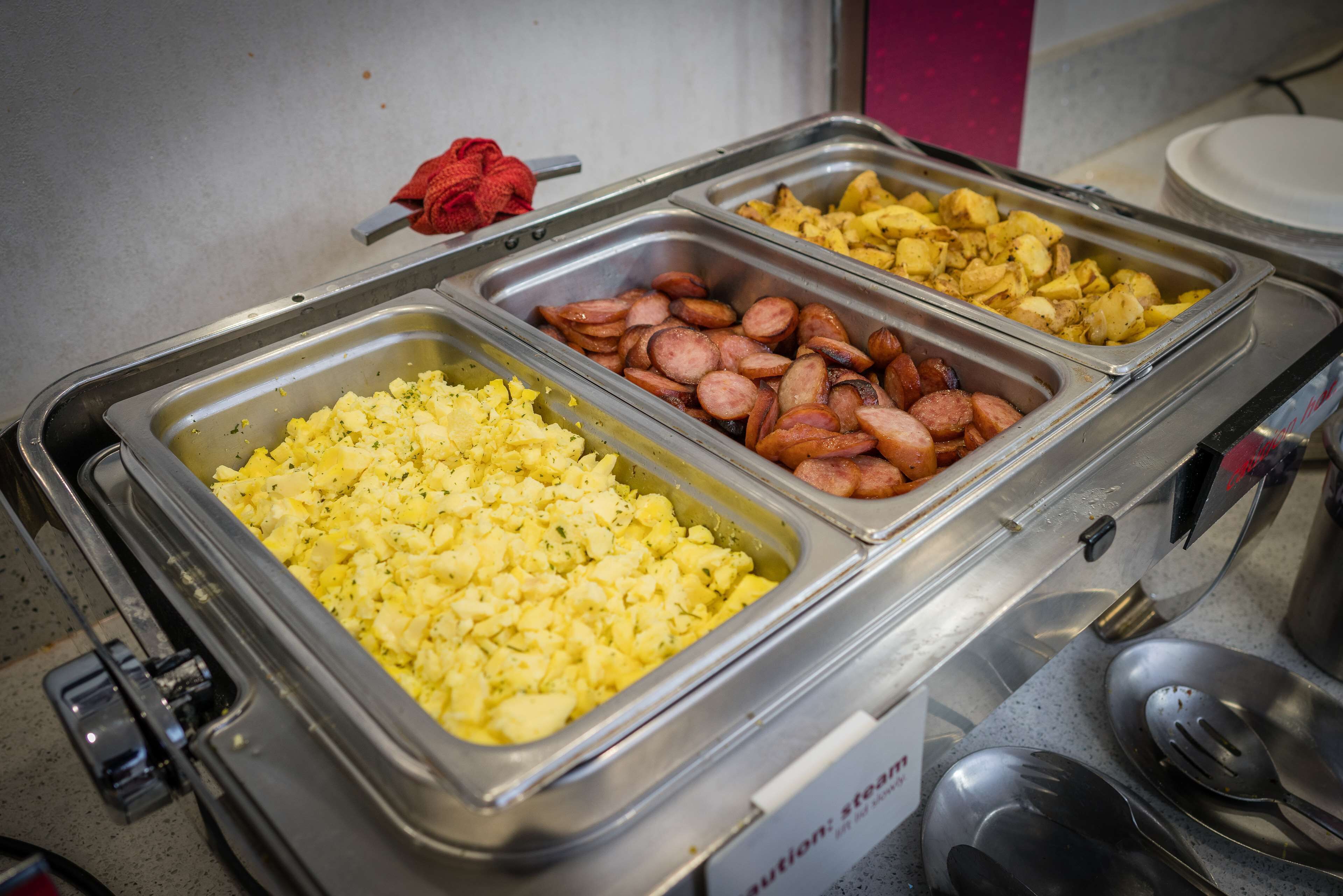 A buffet with scrambled eggs, sliced sausages, and potatoes.