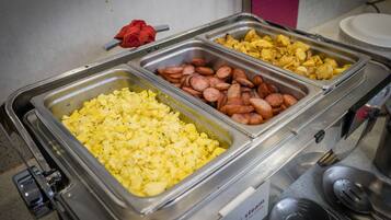 A buffet with scrambled eggs, sliced sausages, and potatoes.