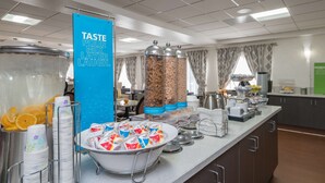 Un espace buffet proposant une variété de plats, notamment un grand récipient rempli de tranches d’orange, des piles d’assiettes en papier et plusieurs distributeurs de condiments.