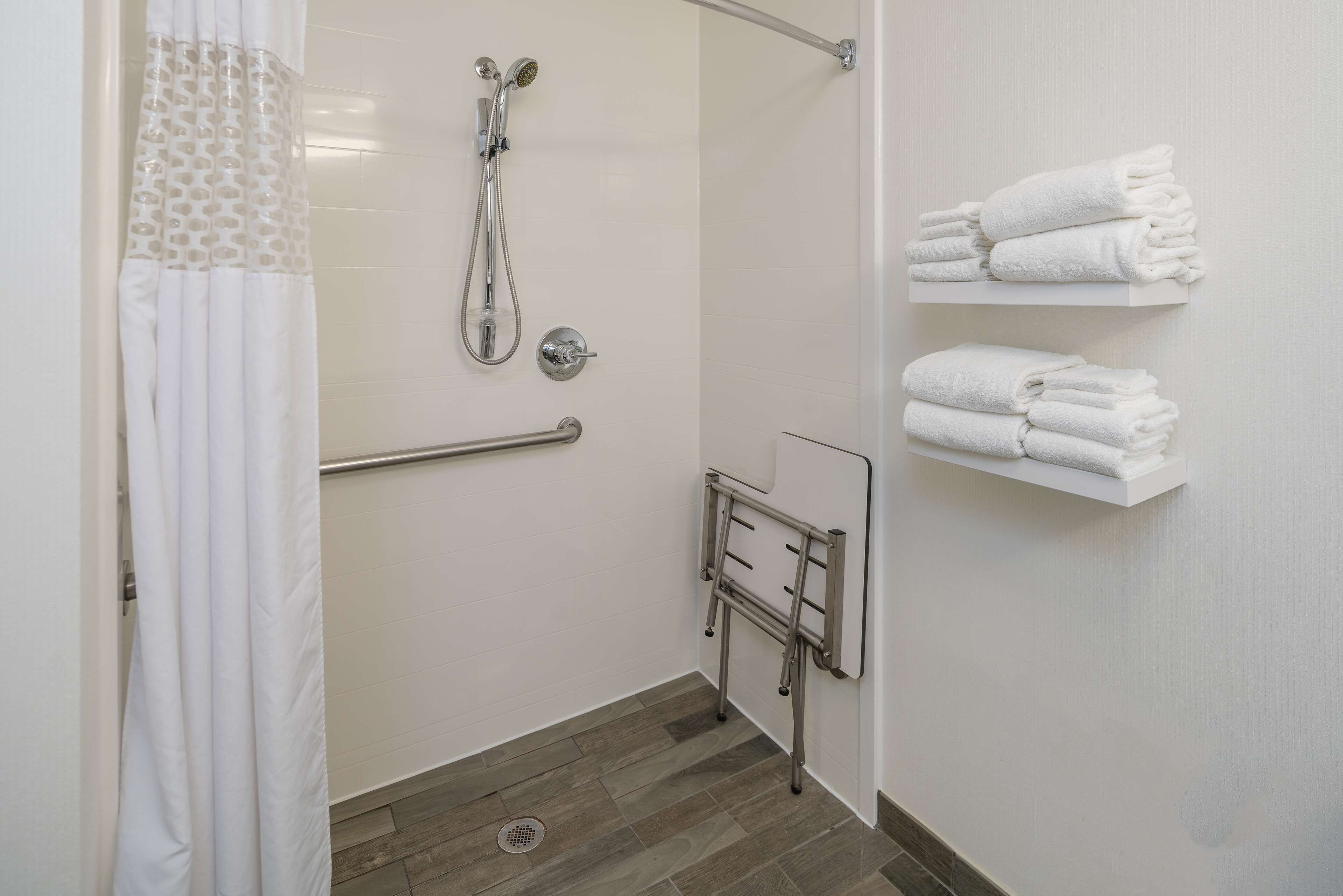 A modern bathroom with a shower, grab bars, and white towel storage.