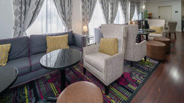 Un hall d’hôtel moderne avec un canapé gris, des fauteuils à motifs, une table basse ronde et un tapis coloré.