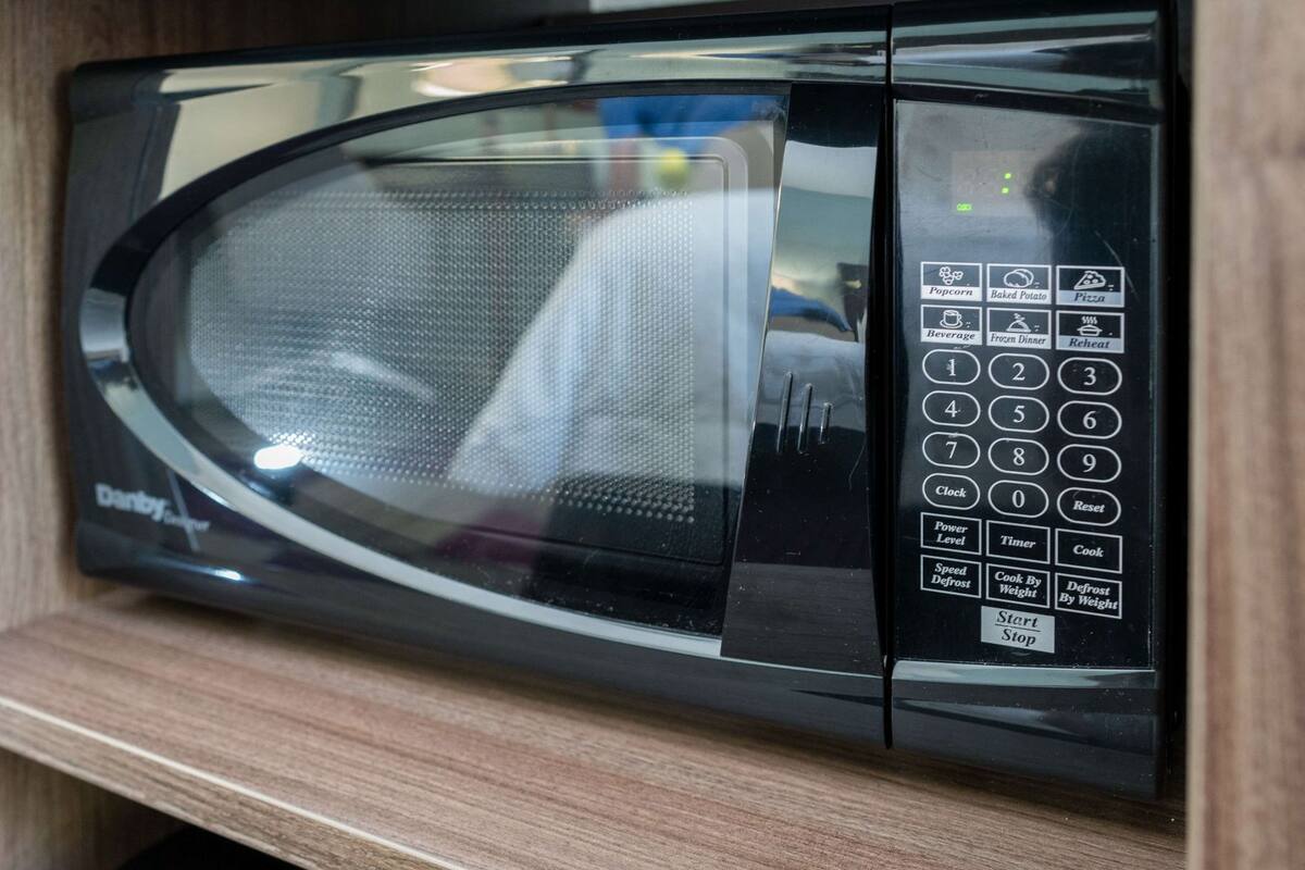 A black microwave oven with a digital control panel, including buttons for popcorn, baked potato, pizza, beverage, frozen dinner, and defrost by weight.