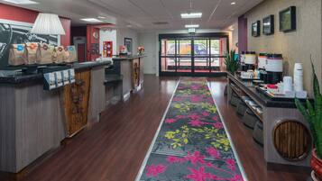 Un hall d’hôtel comprenant un comptoir d’accueil, un espace où l’on peut se servir du café et un tapis à motifs floraux.