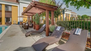 Un espace aménagé au bord de la piscine, avec des chaises longues, une pergola et des plantes en pot.