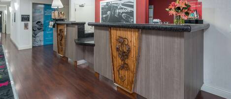 A reception area with a wooden reception desk, a clock on the wall, and a poster advertising a car rental service.