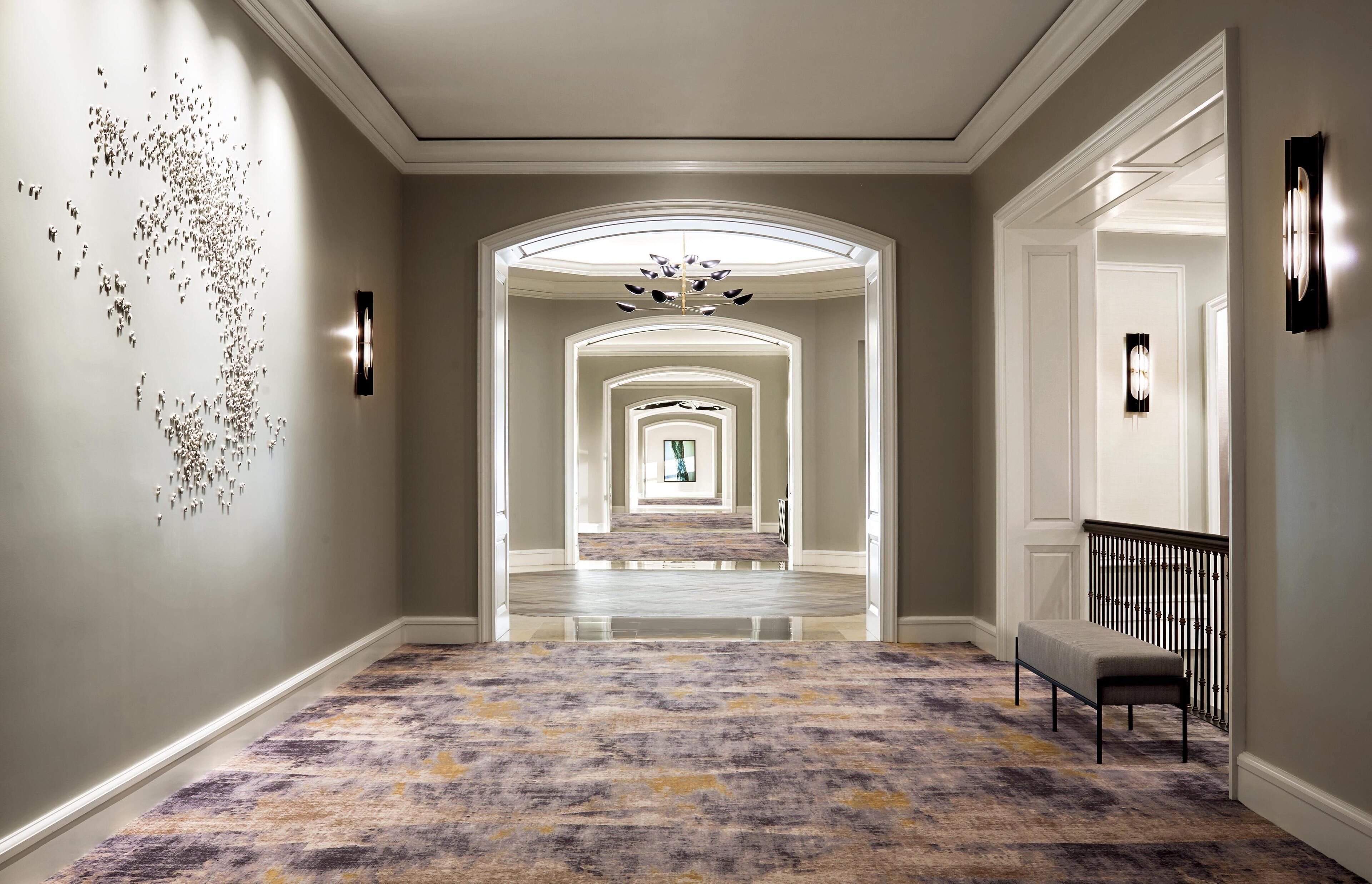 A hallway with a patterned carpet, a bench, and a wall art installation.