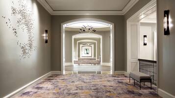 A hallway with a patterned carpet, a bench, and a wall art installation.