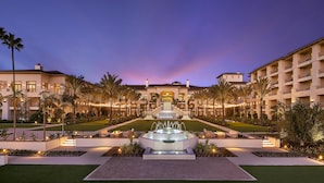 Un hotel con una fuente central, palmeras y un patio bien iluminado.