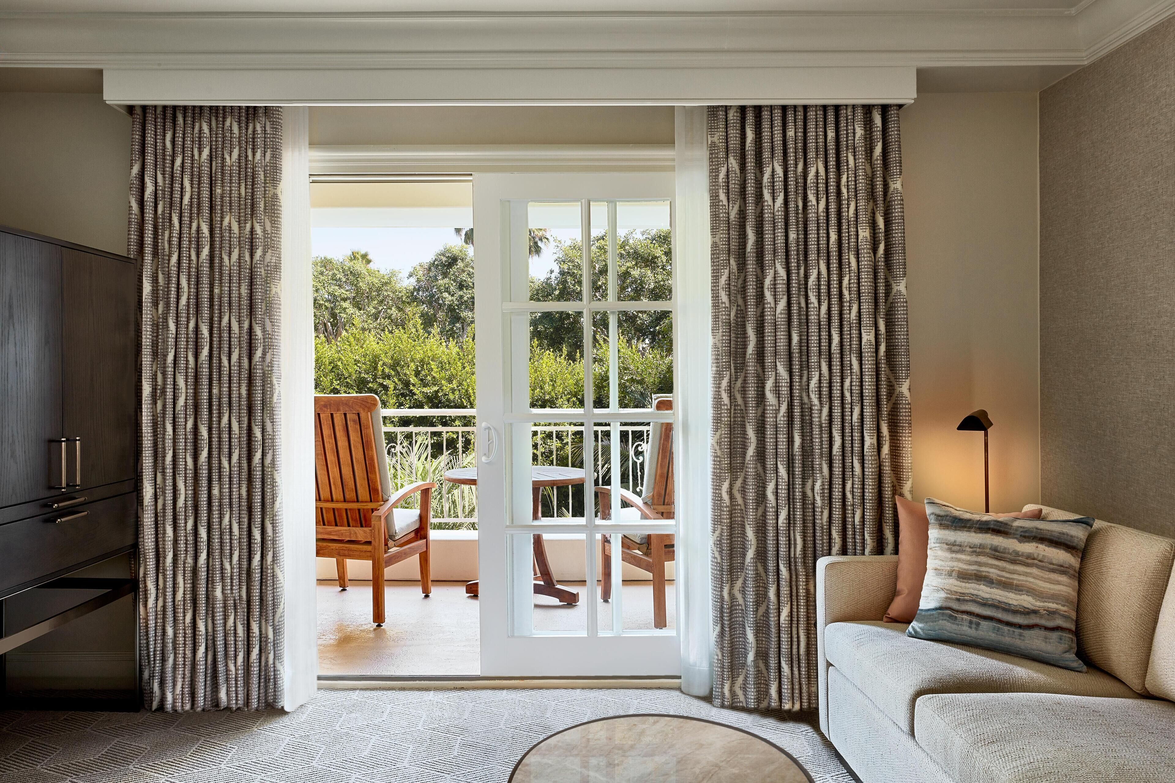 A room with a sofa, a television, and a view of an outdoor balcony with chairs and a table.