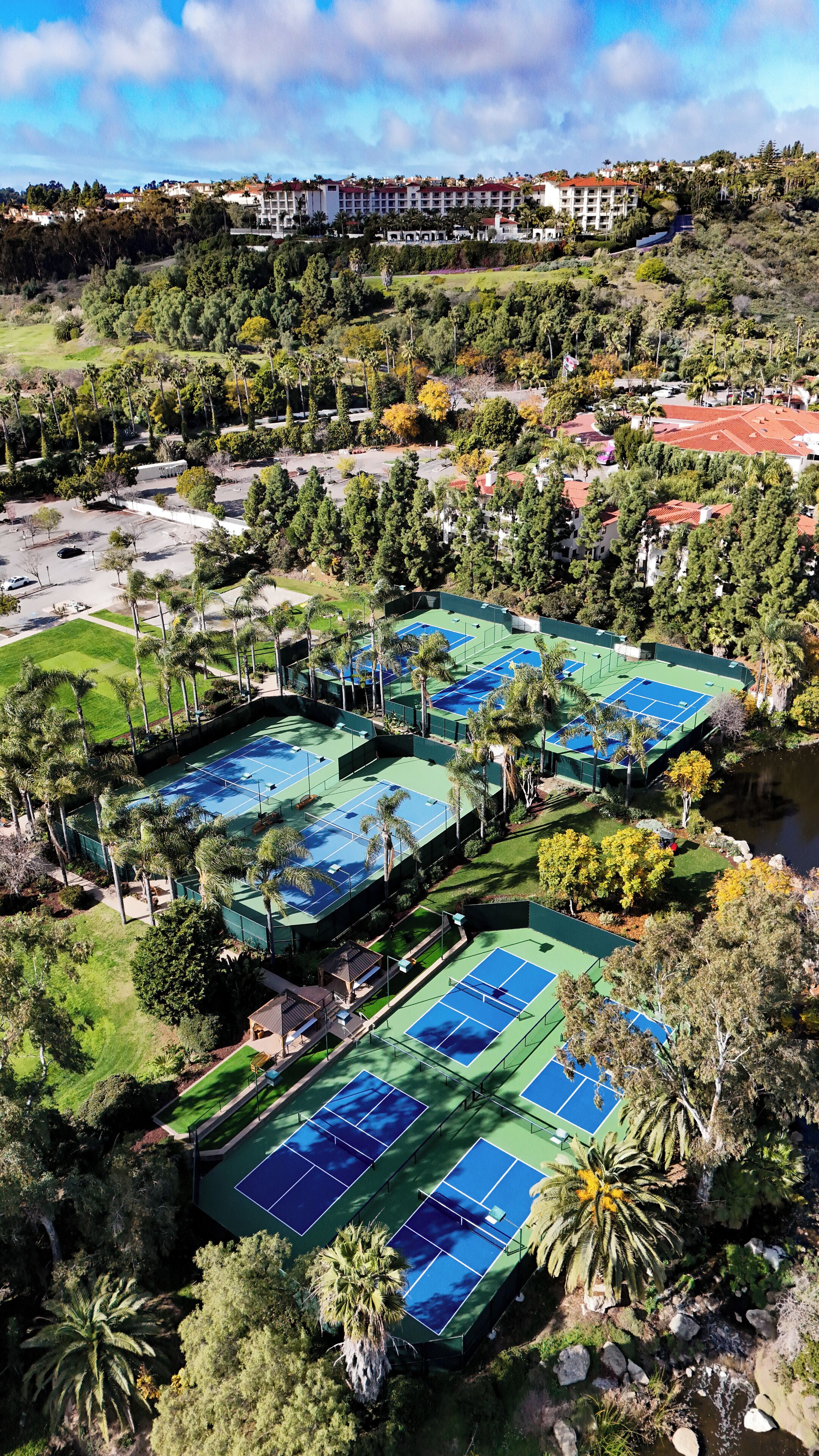 An aerial view of a resort with multiple tennis courts surrounded by lush greenery and palm trees.