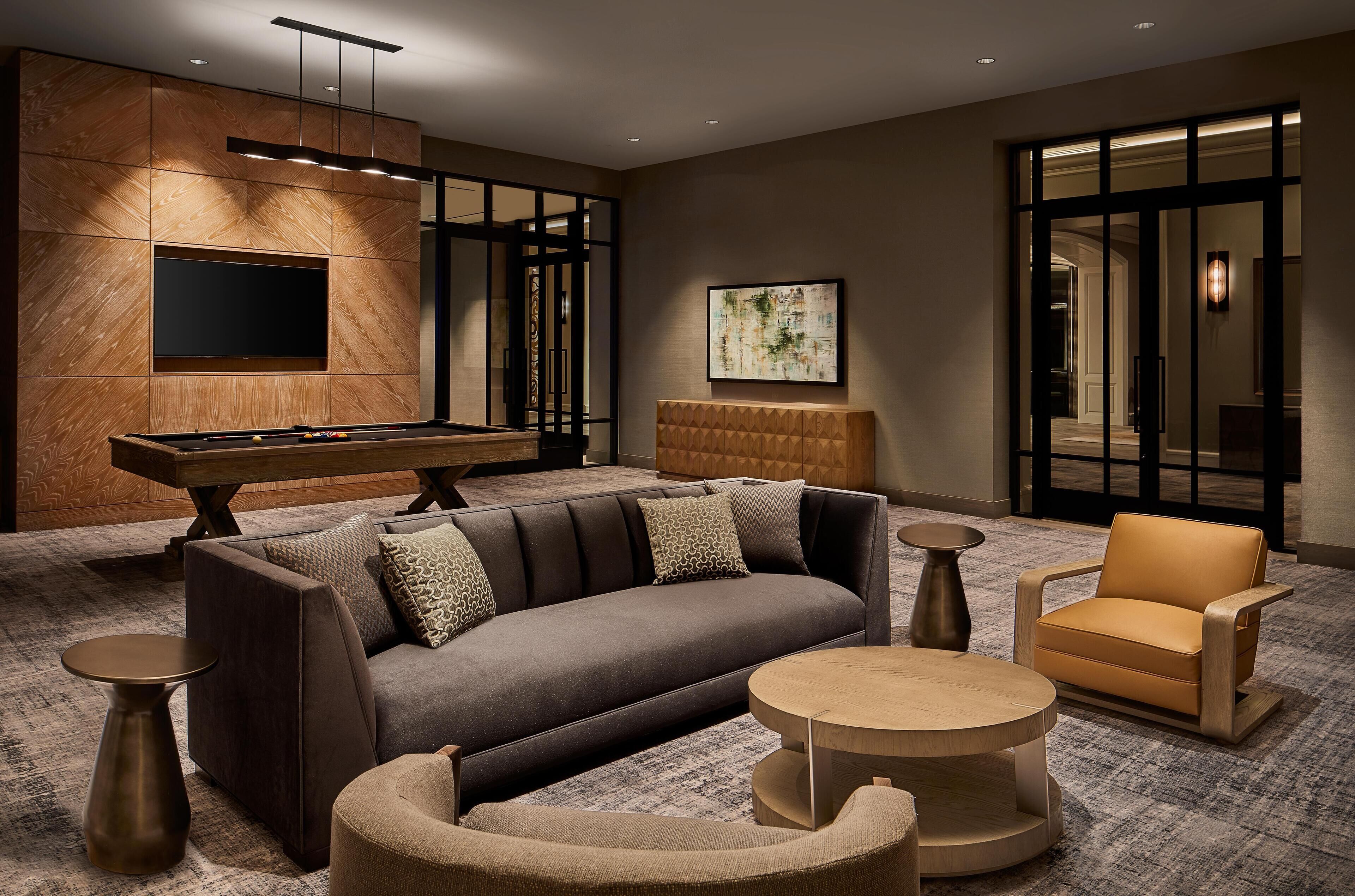 A modern lounge area with a pool table, sofa, armchair, and round coffee table.