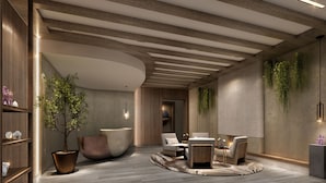Un área de estar moderna con techo de madera, un amplio espacio de asientos con sofás y sillones, una jardinera grande con un árbol y una planta montada en la pared.
