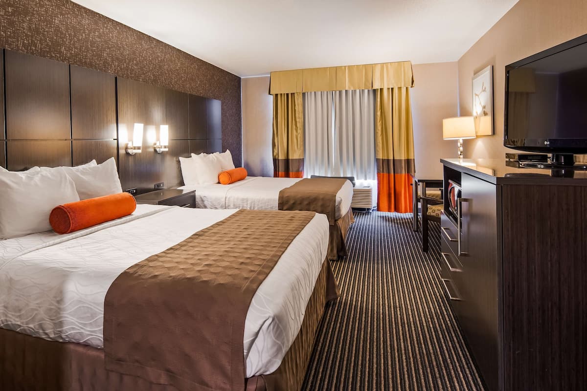 A hotel room with two beds, a TV, a desk, and a large window with curtains.