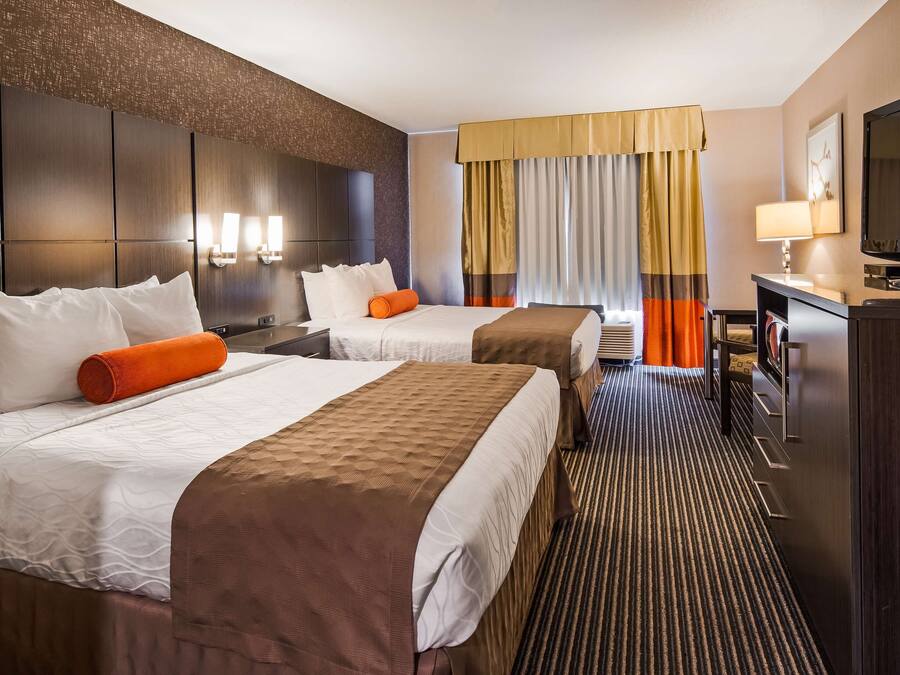 A hotel room with two beds, a TV, a desk, and a large window with curtains.