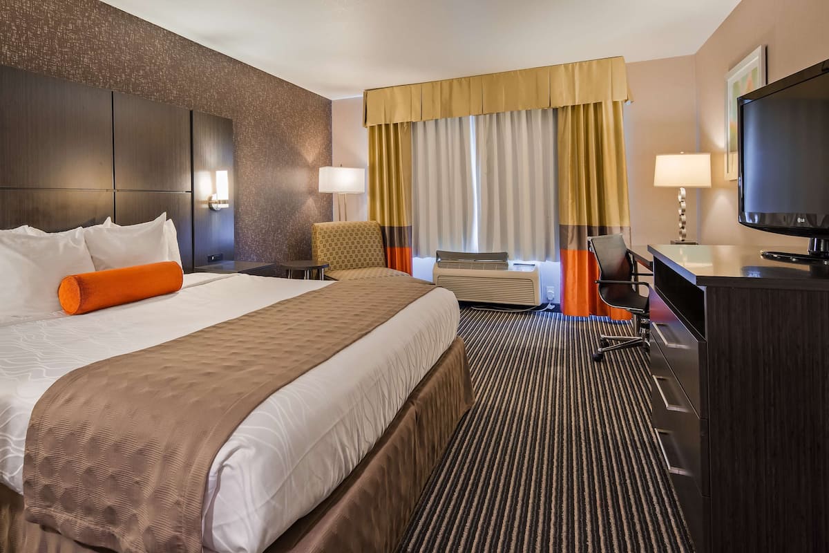 A hotel room with a large bed, a desk, a chair, an air conditioning unit, and a television.