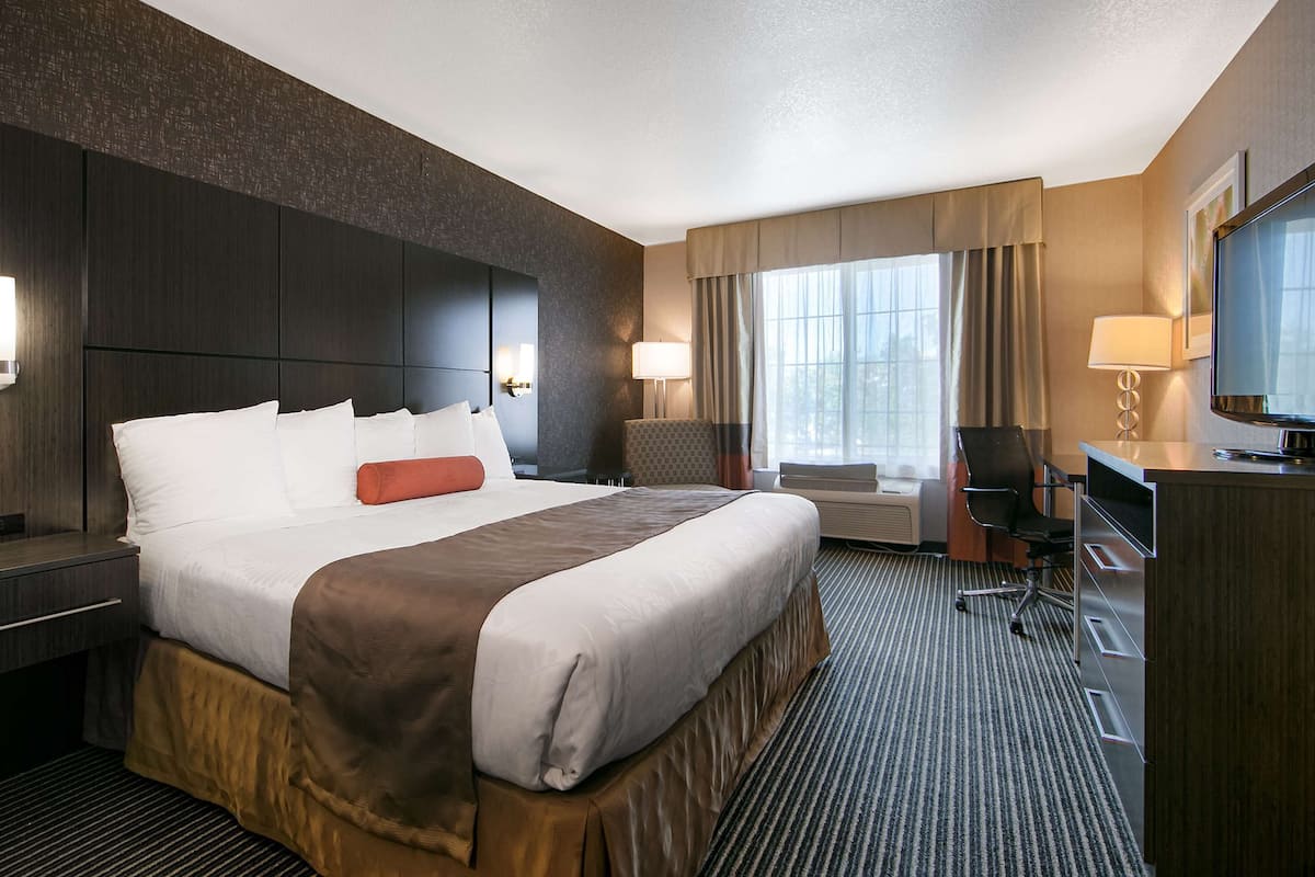 A hotel room with a large bed, a desk, a chair, a television, and a window with curtains.