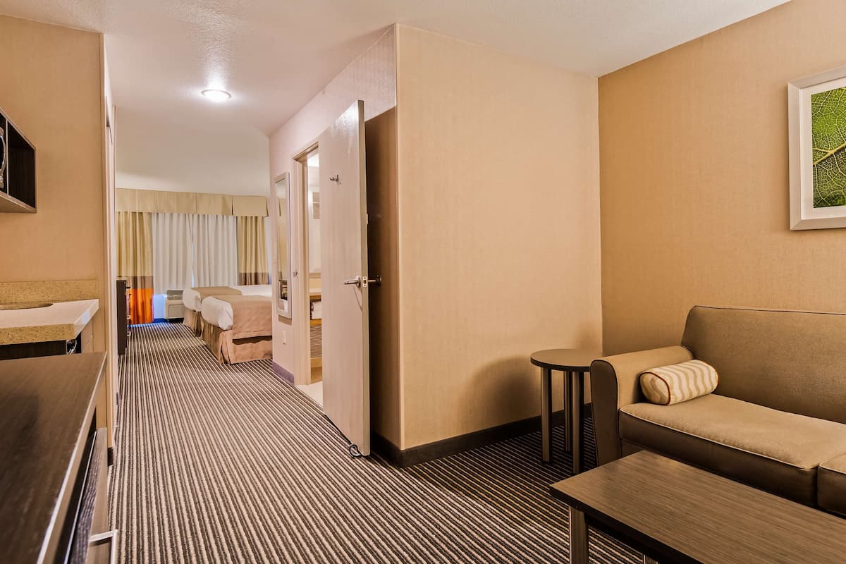 A hotel room with a kitchenette, a sofa, a small table, and a bed with a striped carpet.