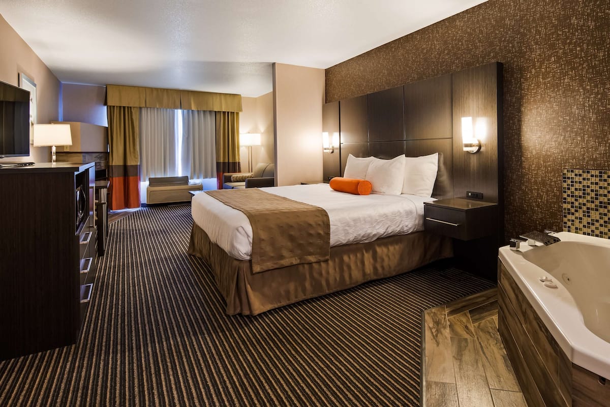 A hotel room with a large bed, a desk, a chair, a desk lamp, a TV, a bathroom with a bathtub, and a shower.