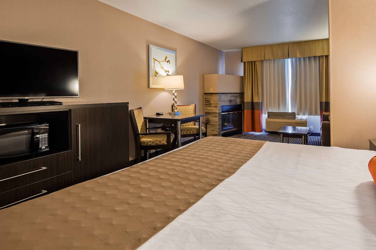 A hotel room with a bed, a desk, a television, a fireplace, and a window with curtains.