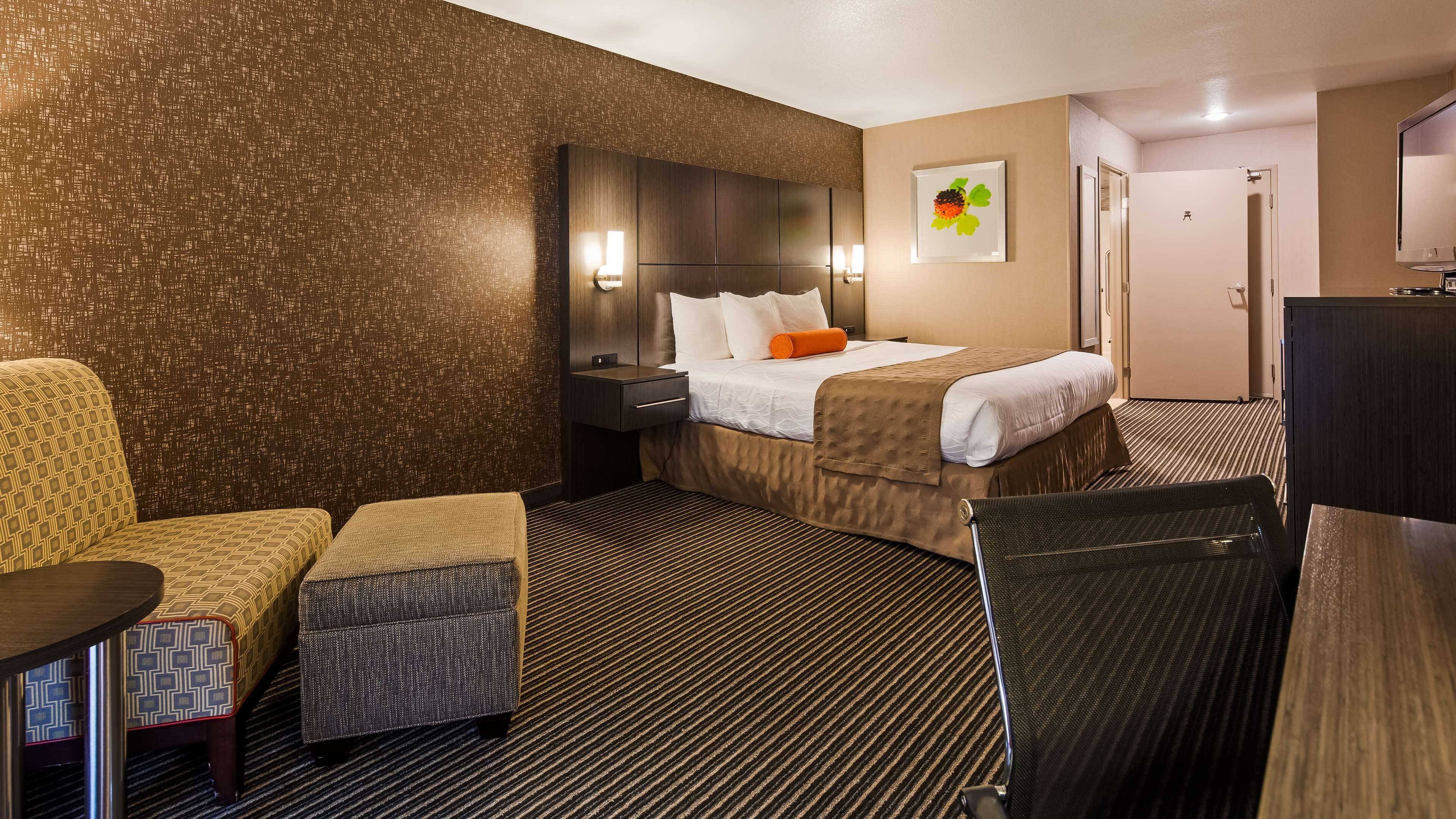 Een hotelkamer met een bed, twee fauteuils, een tafeltje, een bureau en een televisie.
