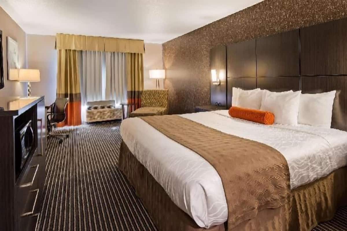 A hotel room with a large bed, a desk with a lamp, a chair, a wardrobe, and a large mirror.