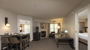 A hotel room with a dining area, a sofa, a small table with a lamp, and a fireplace.