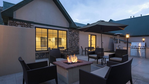 An outdoor patio area with a fire pit, wicker furniture, a stone wall, and a kitchen area with a grill.