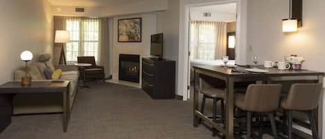 A hotel room with a sofa, a dining table with chairs, a fireplace, a TV, and a wall-mounted light fixture.